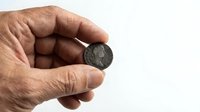 Senior man hand holding ancient Roman coin showing historical numismatic collection piece for educational and archaeological study purposes.
