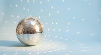 Shiny disco ball reflecting light spots on pale blue background creating festive party atmosphere for celebrations and entertainment events.
