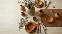 Rustic terracotta dinnerware set with olive branches on neutral linen table runner, perfect for organic dining and Mediterranean-inspired table styling.