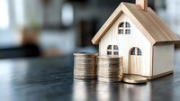 Wooden house model with stacked coins on dark surface representing real estate investment, mortgage planning, property savings and home financing concepts.