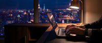 Professional working late at night on laptop with illuminated city skyline view through office window for business and technology concepts.