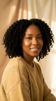 Young African American woman with natural curly hair smiling warmly in cozy beige sweater against soft golden lighting for lifestyle and portrait photography.