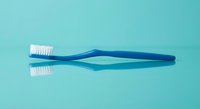 Blue toothbrush with white bristles on turquoise background for dental hygiene and oral care concepts.