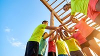 Construction workers in bright safety vests collaborating on wooden roof frame structure against blue sky. Teamwork and cooperation in building industry.