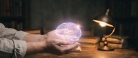 Hands holding glowing pink brain hologram above wooden desk with vintage lamp in dark library setting for neuroscience and mental health concepts.