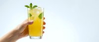 Hand holding refreshing orange cocktail with mint garnish and ice cubes against clean white background for beverage marketing and summer drink concepts.