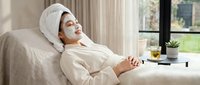 Young woman relaxing in bathrobe with facial mask at home spa enjoying self-care wellness routine for skincare and beauty treatment relaxation.