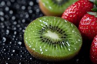 Fresh juicy kiwi slice and ripe strawberries on dark background with water drops. Macro food photography showing texture and details of tropical fruits.
