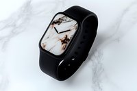 Modern smartwatch with marble pattern display face and black silicone band on white marble background, showcasing luxury tech accessory design.
