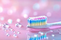 Pink toothbrush with colorful bristles on reflective surface with water drops and soft bokeh background in pastel colors, dental hygiene concept.