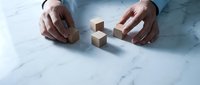Businessman hands arranging wooden cube blocks on marble desk surface for strategic planning and problem solving in corporate environment.
