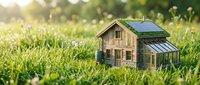 Miniature wooden house model with solar panels sits in green grass field with soft sunlight, representing eco-friendly sustainable living and green energy concepts.