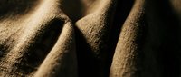 Closeup of natural woven fabric texture with warm golden tones and deep shadows, showcasing detailed fiber patterns and weave structure for textile design projects.