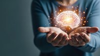 Glowing brain hologram floating above cupped hands with sparkling light effects representing artificial intelligence, innovation and mental power concepts.