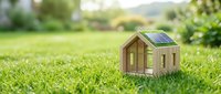 Eco-friendly wooden house model with solar panel on green grass outdoors representing sustainable energy and green building concepts for environmental design.