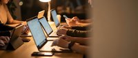 Business team working late at office with laptops and smartphones in warm evening light for productivity and collaboration projects.