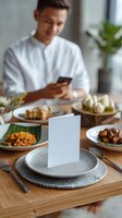 Asian man in white shirt using smartphone at dining table with blank menu card on plate, traditional dishes and modern table setting for restaurant promotion.