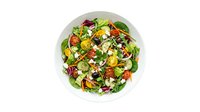 Fresh mixed green salad with roasted vegetables, seeds and cheese on white plate, isolated on white background for food and nutrition design use.