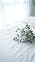 Fresh eucalyptus and white flower bouquet on white bedding in bright bedroom with natural window light for home decor and lifestyle photography.