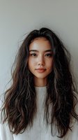 Young Asian woman with flowing dark hair wearing white sweater against light background, natural makeup and gentle smile creating modern minimalist portrait.