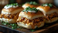 Pulled pork sliders with barbecue sauce on soft brioche buns, garnished with fresh herbs and onions, served on wooden board.