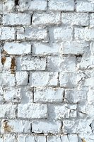 Roughly painted white brick wall with peeling paint and weathered texture showing aged character and rustic architectural detail. Background for urban design.