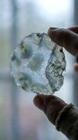 Hand holding translucent moss agate slice with natural green inclusions against soft blurred background for geology education and mineral collection display.