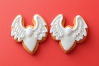 Two white angel wing cookies with royal icing on coral background. Holiday baking, Christmas treats, religious celebration desserts for festive occasions.