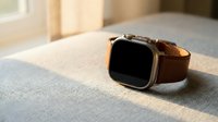 Modern smartwatch with brown leather strap on minimalist surface in warm natural lighting for technology and lifestyle concepts.