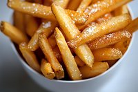 Golden crispy french fries served in white ceramic bowl, close-up view showing texture and seasoning. Fresh hot potato strips with salt for restaurant menu.