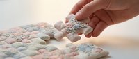 Hand placing final puzzle piece into completed pastel-colored jigsaw puzzle, symbolizing problem-solving, achievement, and business success for marketing and educational content.