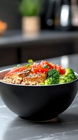 Asian-inspired salmon bowl with brown rice, fresh broccoli, red bell peppers, and sesame seeds served in black ceramic bowl on marble counter.