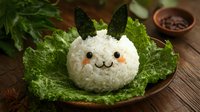 Cute bunny shaped rice ball with nori ears on green lettuce leaf. Creative Asian food styling with kawaii animal face made from white rice and seaweed on wooden table.