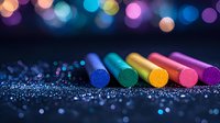 Colorful chalk pastels arranged in row on dark background with glitter and bokeh lights creating magical artistic atmosphere. For creative design projects.