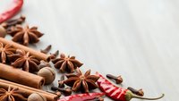 Aromatic winter spices including cinnamon sticks, star anise, coffee beans and red chili peppers arranged on rustic wooden background for cooking.