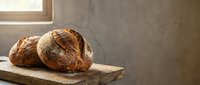 Freshly baked artisan bread loaves with golden crust on rustic wooden cutting board in warm kitchen setting with natural sunlight streaming through window.