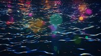 Colorful bokeh lights reflecting on rippling water surface creating magical nighttime atmosphere with blue, purple, and golden glowing spots.