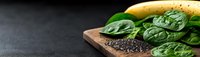 Fresh spinach leaves and chia seeds on wooden cutting board against dark background, panoramic food composition with copy space for healthy eating concept.