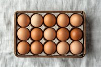 Fresh brown chicken eggs arranged in cardboard container on light linen tablecloth background, top view composition for food photography and packaging.