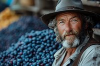 Mature bearded farmer with gray hair and hat smiling near fresh harvested blueberries at local market, authentic portrait in natural lighting shows agricultural lifestyle.