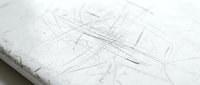 Scratched white surface with multiple intersecting lines and marks creating abstract texture for backgrounds and design projects.