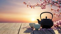 Traditional cast iron teapot with ceramic cup on wooden table during cherry blossom season at sunset for peaceful tea ceremony and mindfulness moments.