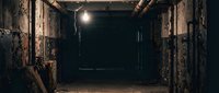 Dark underground tunnel with rusty metal doors and single light bulb illuminating abandoned industrial corridor. Suitable for horror, mystery, thriller projects.
