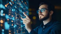 Young Asian professional in glasses analyzing digital data visualization on virtual screen, working with financial charts and business analytics in dark office.