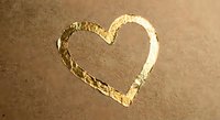 Golden heart shape drawn in sand with textured surface and warm lighting creating romantic beach atmosphere for love and relationship concepts.