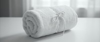 Rolled white towel tied with a ribbon bow on a table, monochrome spa and hotel bathroom concept for wellness and hygiene.