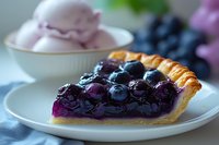 Slice of fresh blueberry pie with juicy whole berries on white plate, served with pink ice cream dessert, close-up view showing flaky golden crust.