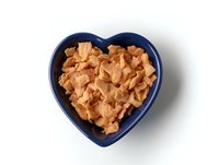 Crispy corn flakes cereal in blue heart shaped ceramic bowl on white background, overhead view, isolated food photography for breakfast and healthy eating concepts.