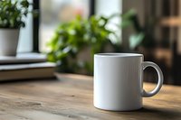 White ceramic coffee mug mockup on wooden table with green plants and books in blurred background, natural lighting creates cozy atmosphere for branding design.