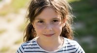 Young Caucasian girl with freckles and braided hair smiling outdoors in striped shirt on sunny day for family lifestyle and childhood concepts.